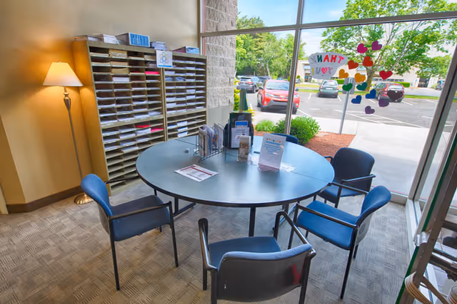 Round table with four chairs in a lobby area beside a windowed wall.