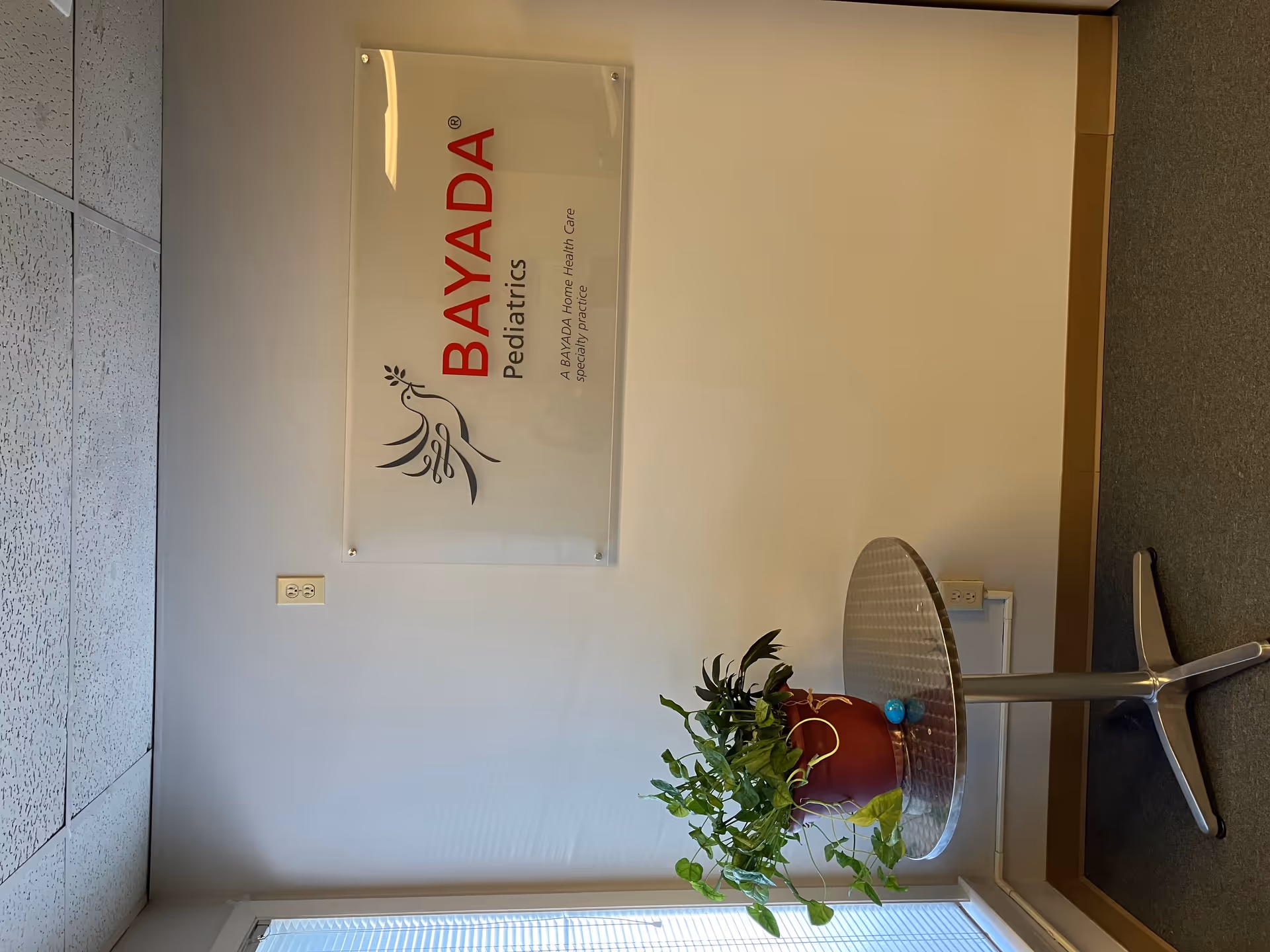 Interior hallway with BAYADA Pediatrics sign and potted plant on a metal stand.