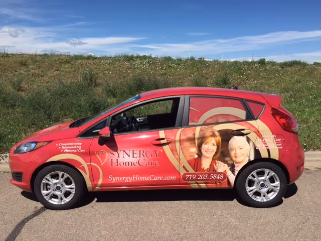 Red SYNERGY HomeCare van with advertising graphics parked on a road.