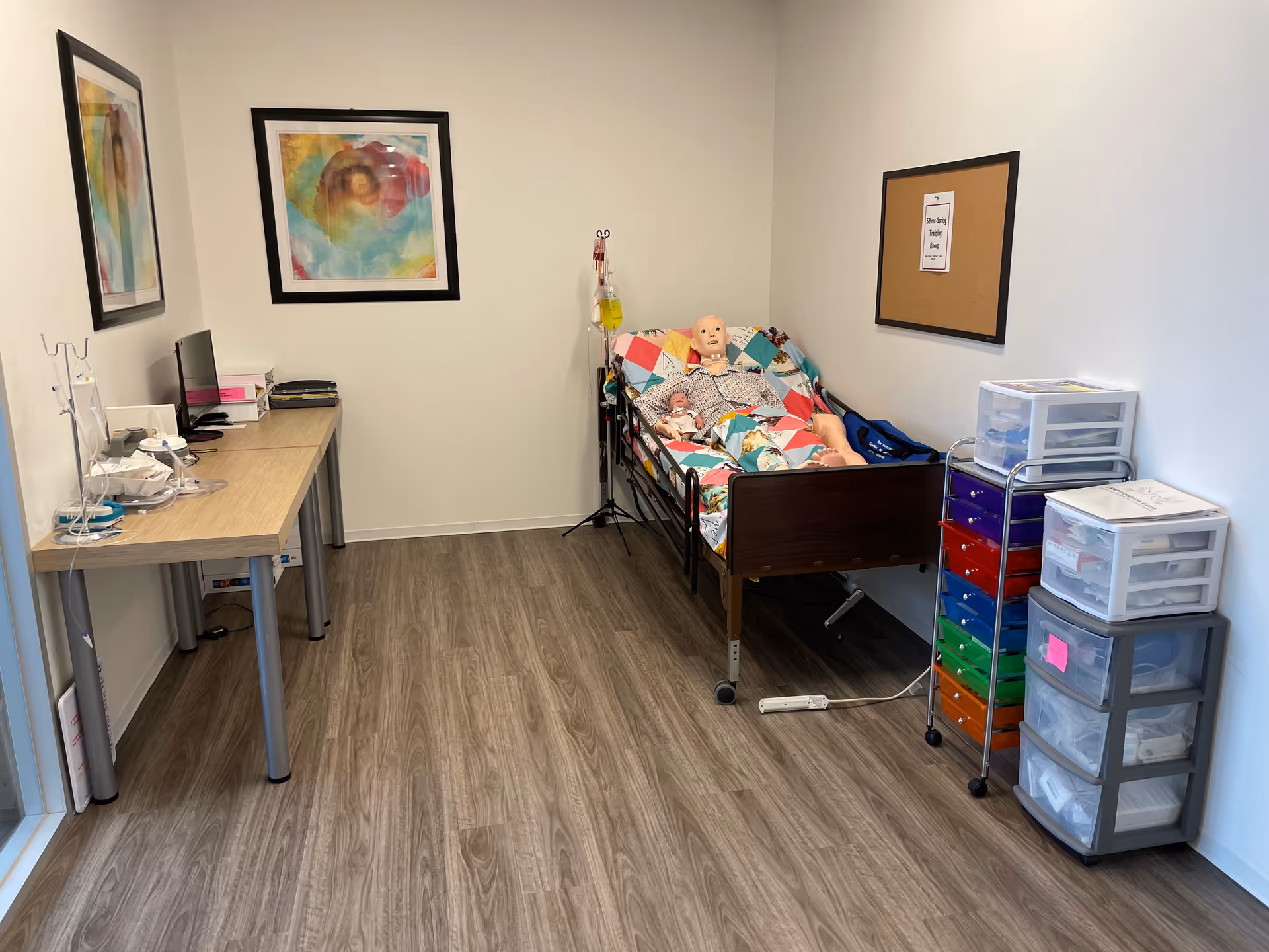 A small hospital-style patient room with a bed, desk, and colorful storage drawers.