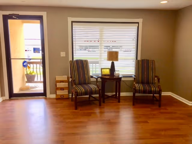 Striped armchairs flank a small table with a lamp near a window in living room.