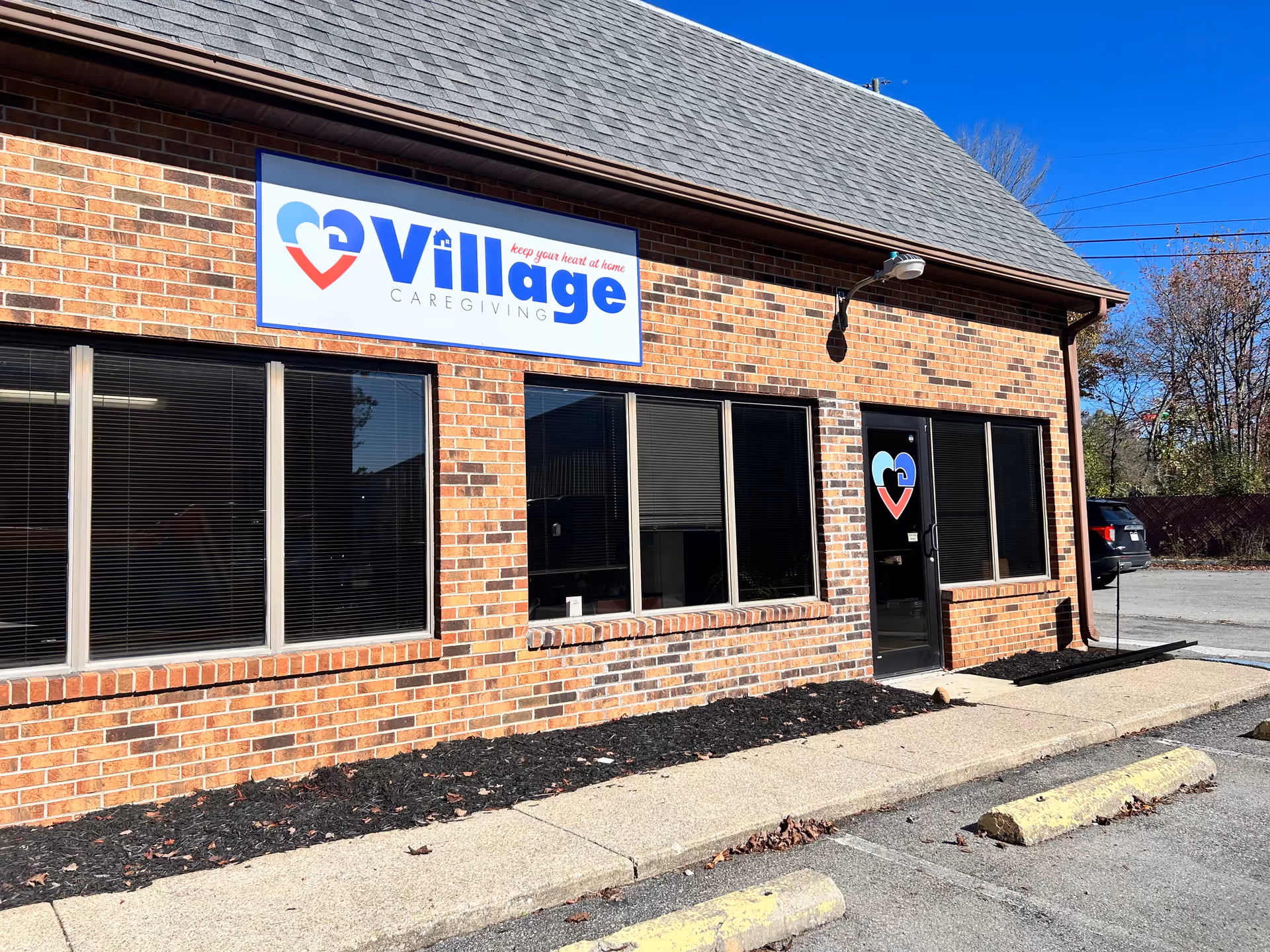 Brick building exterior with Village Caregiving sign and large windows under a blue sky