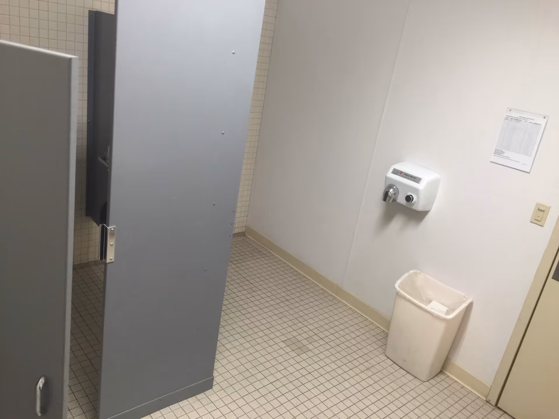 Public bathroom with tiled floor, tall gray stalls, and a wall-mounted hand dryer.