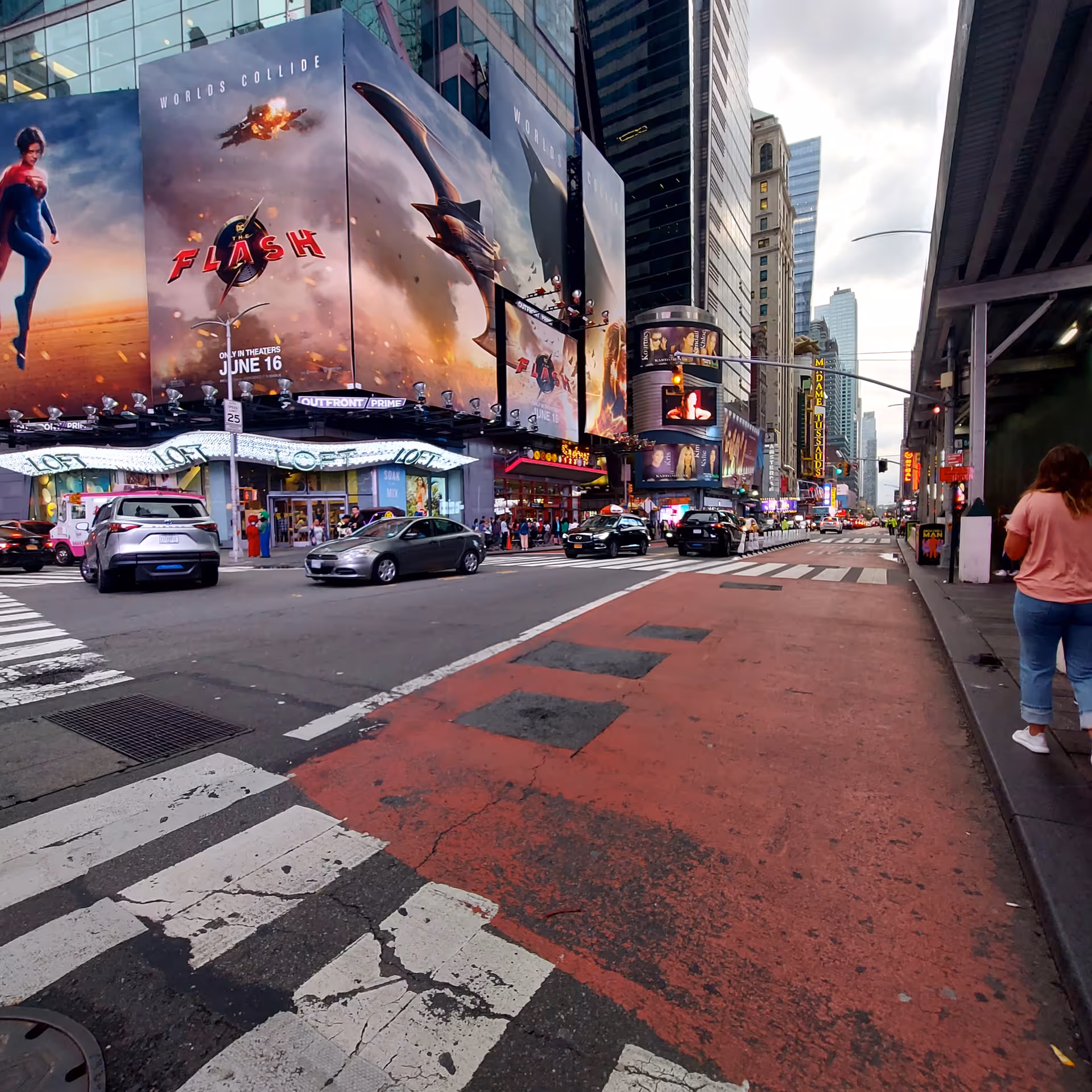 Busy city street with large movie billboards and cars, pedestrians along storefronts.