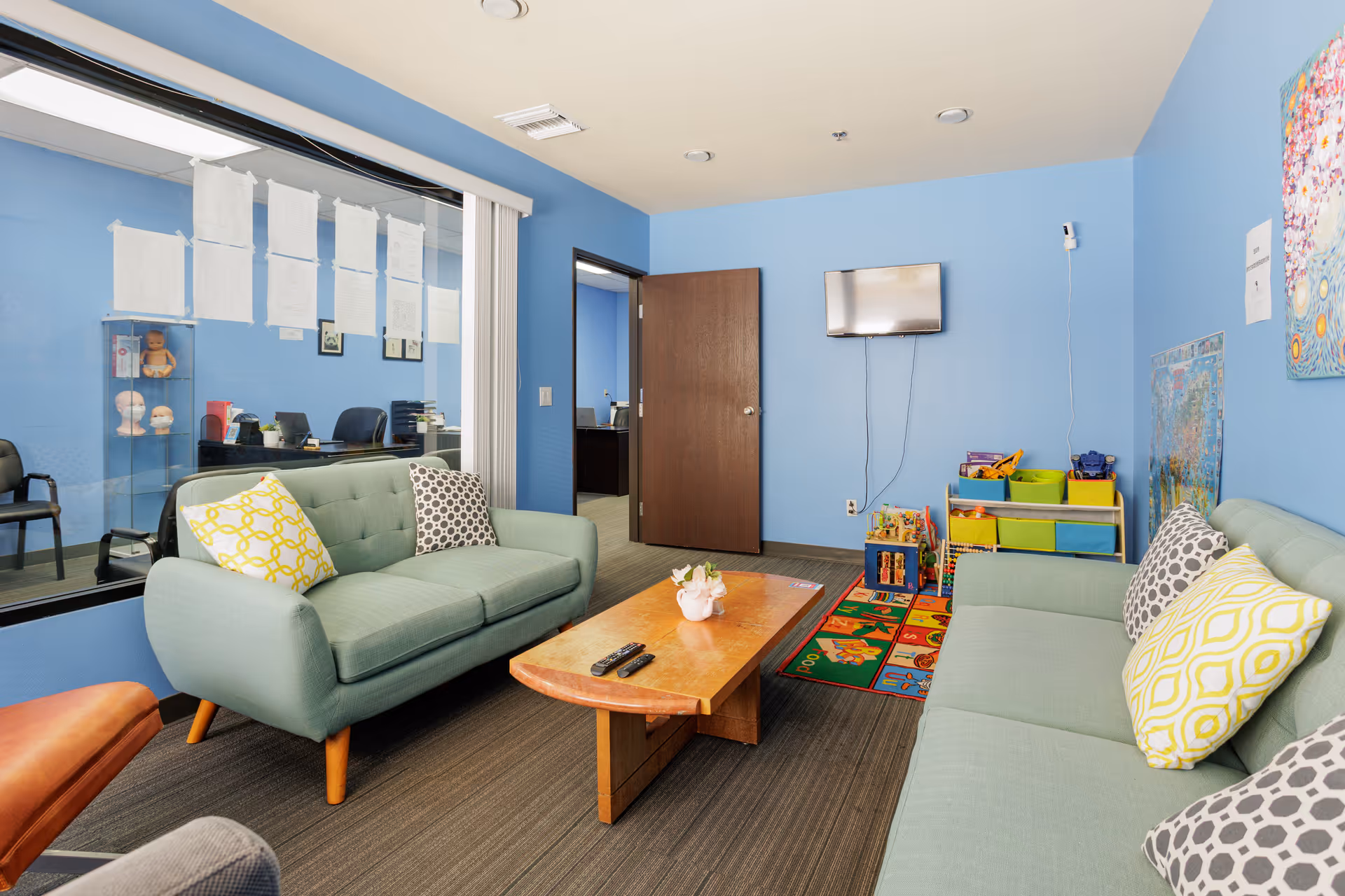Blue-walled lounge with teal sofas, a coffee table, and a children's play area.
