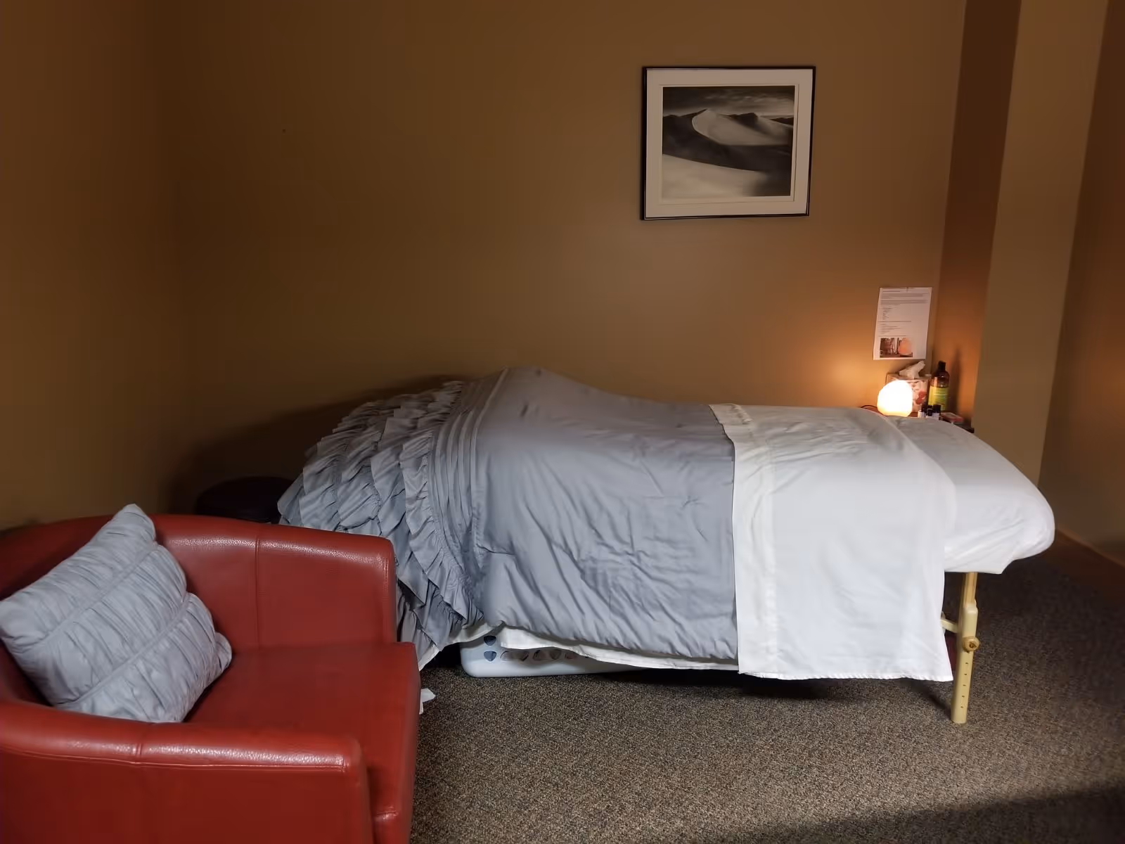 A small beige bedroom with a neatly made bed and a red armchair.