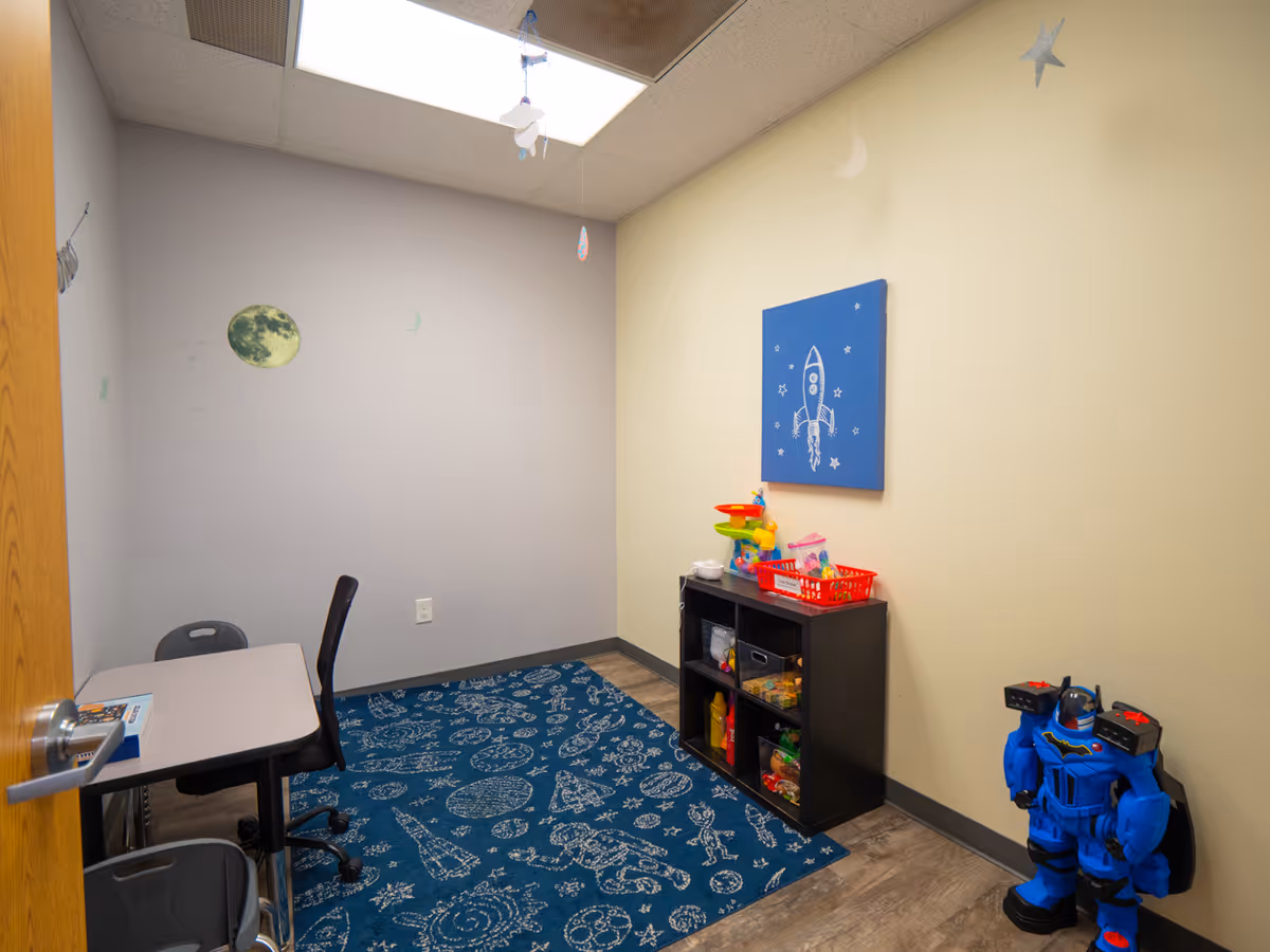 Small children's play area with table, chairs, toy shelf, rug, space-themed decor.