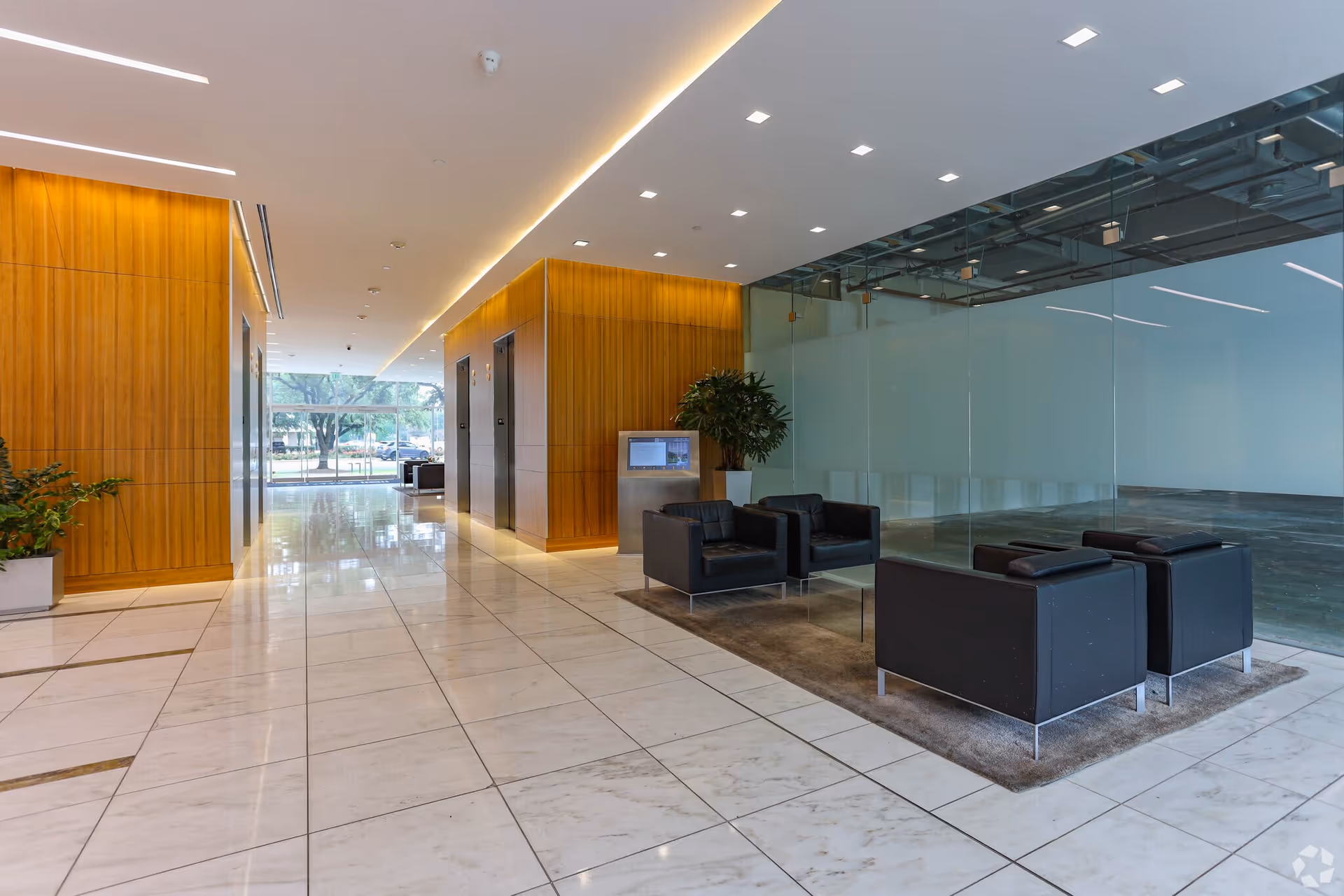 Marble-tiled lobby with wooden wall panels, glass partitions, black lounge chairs, and plants.