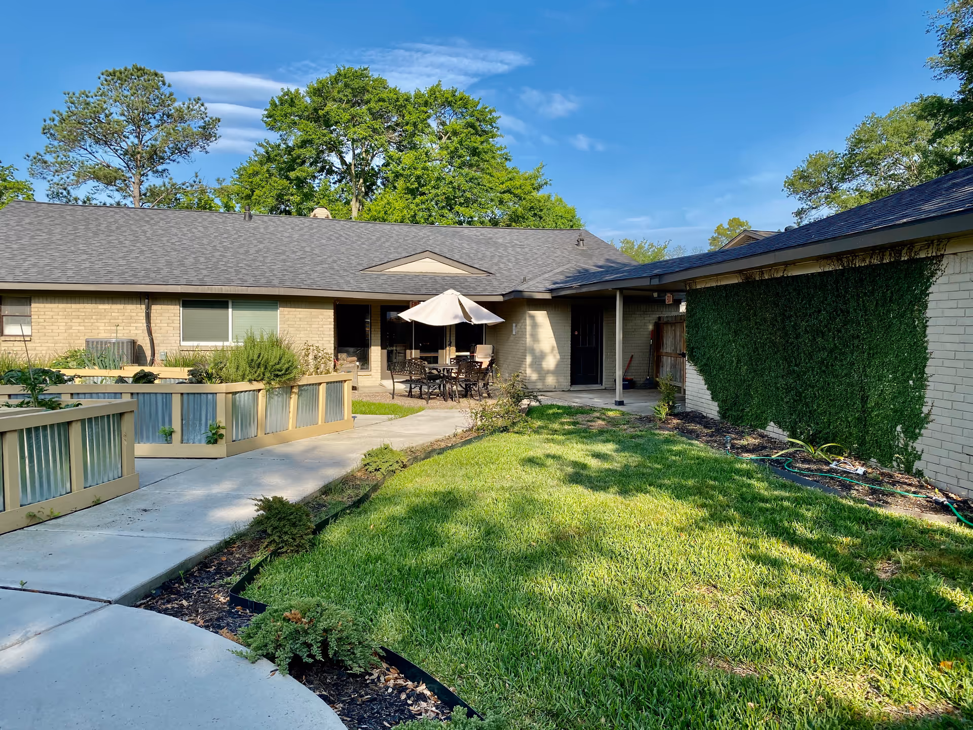 Single-story facility exterior with a courtyard patio, umbrella, table, and green lawn.