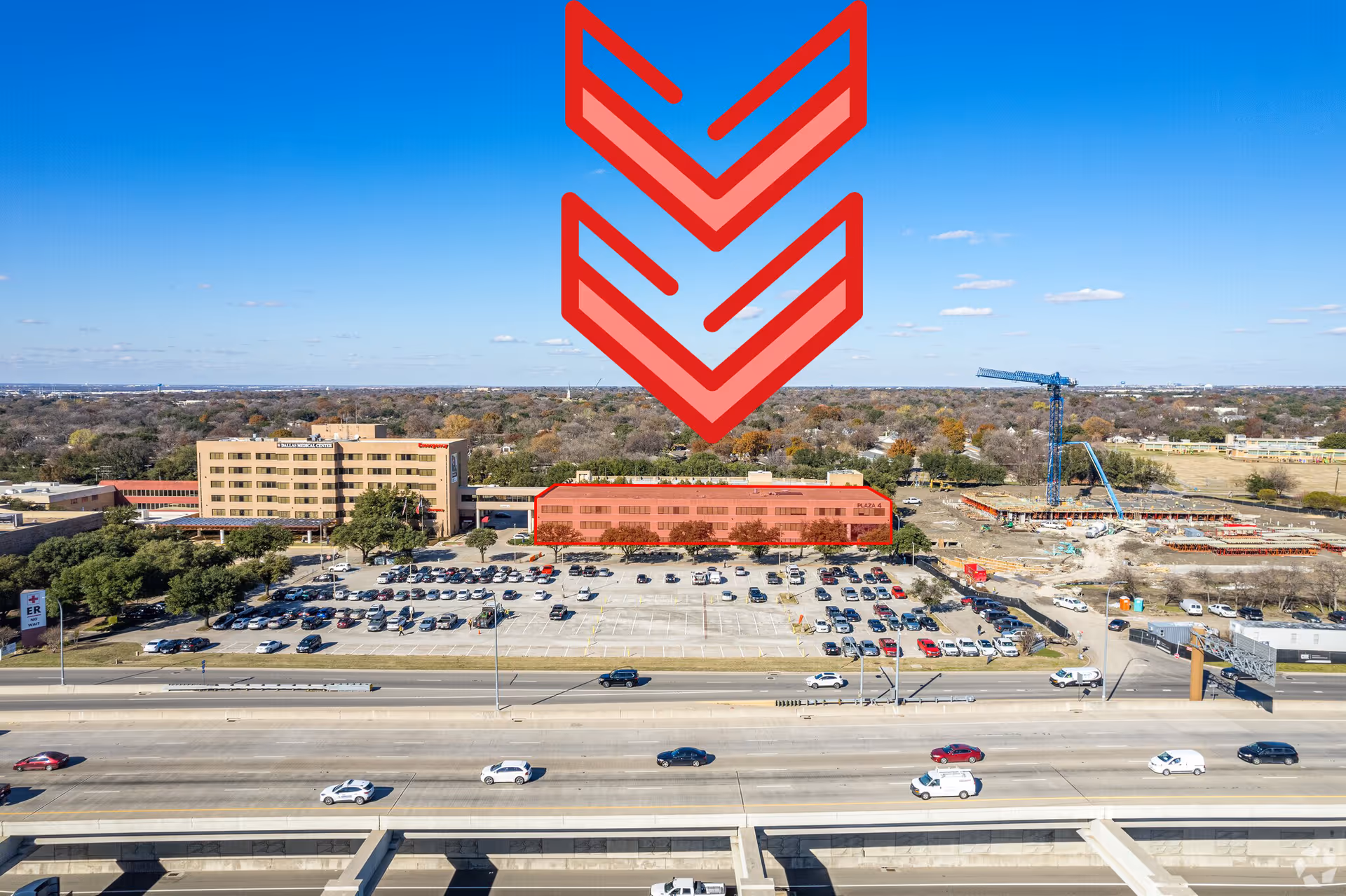 Aerial view of a medical clinic building with parking lots, a highway, and a construction crane.