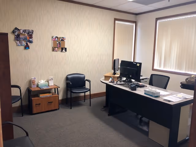 Office space with desk, computers, chairs, and wall photo collages in a reception-like room.