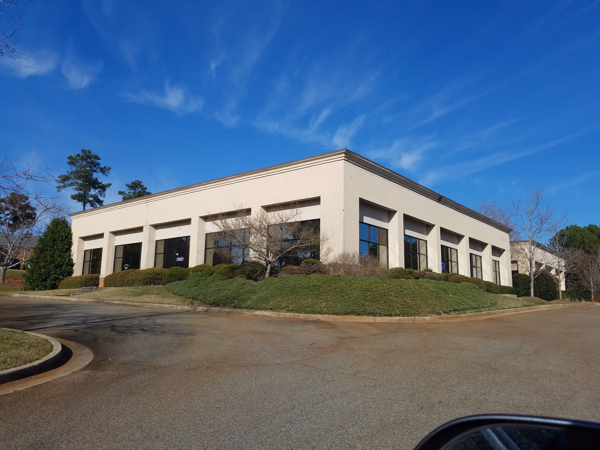 Modern, single-story building with tall windows and landscaped hedges beside a parking lot.