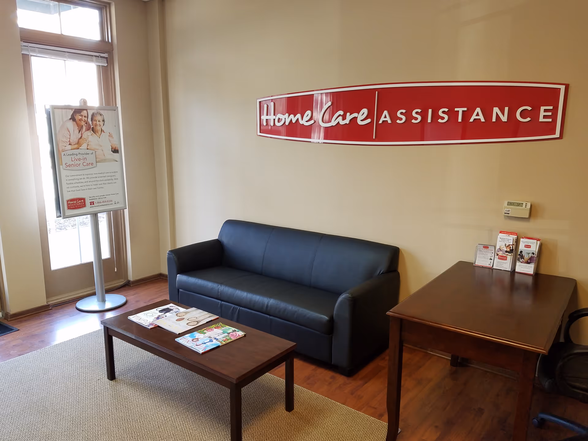 A lobby seating area with a blue sofa, wooden desk, and brochures near Home Care sign.