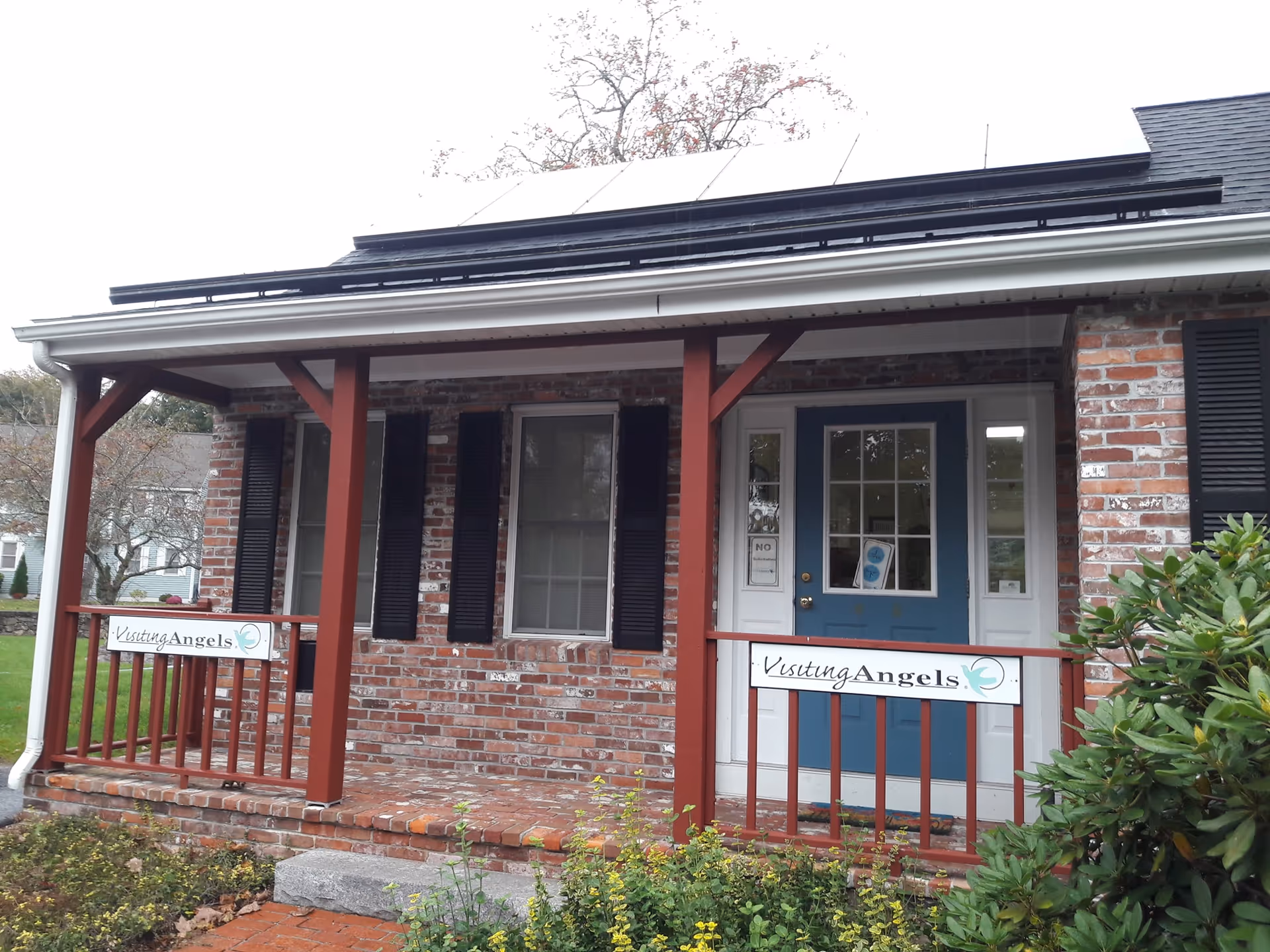 Brick building with a covered front porch, blue door, and Visiting Angels signs.