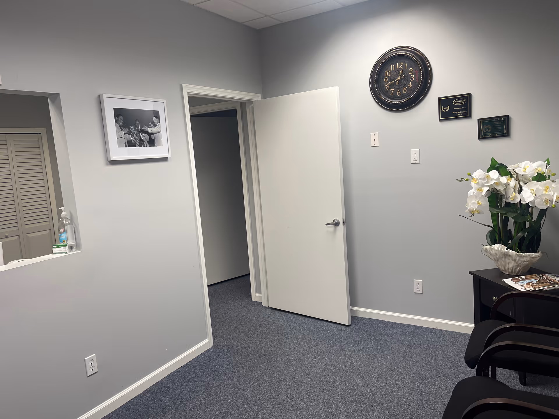 Interior hallway of a senior living facility featuring a wall clock, plant, and seating.