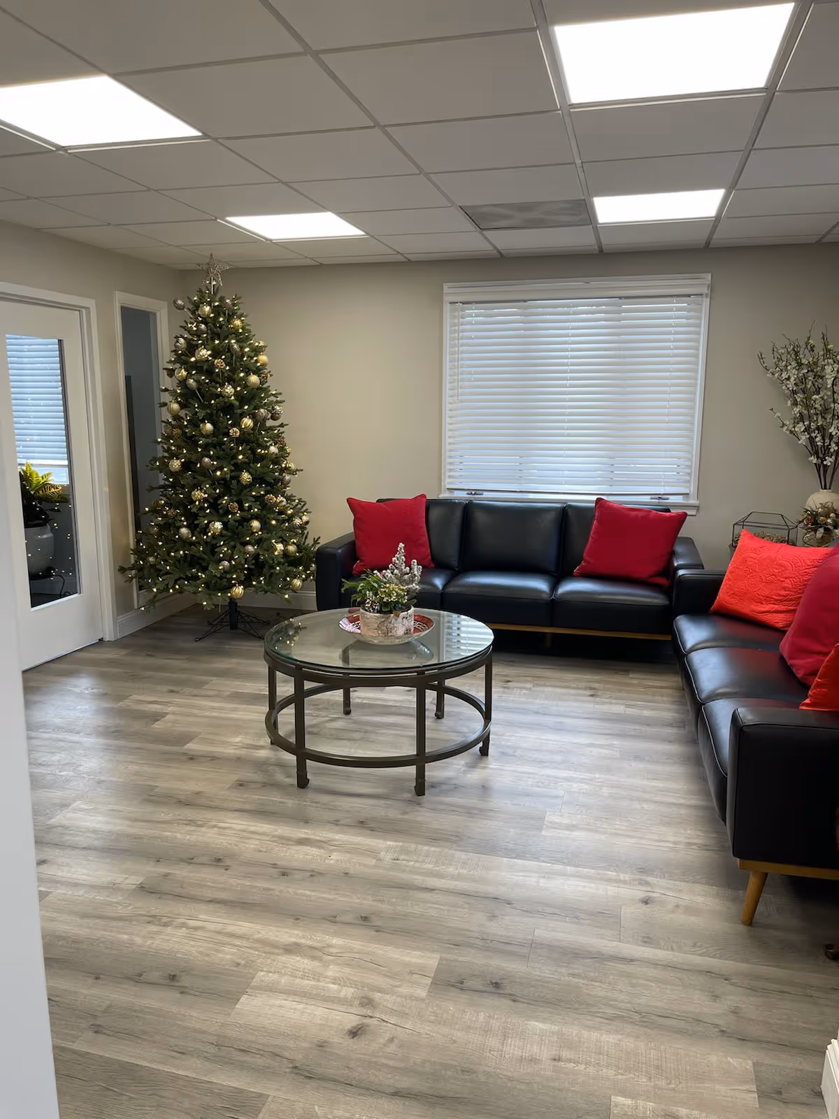 Holiday-decorated living room with a Christmas tree, red cushions, and black leather sofas.
