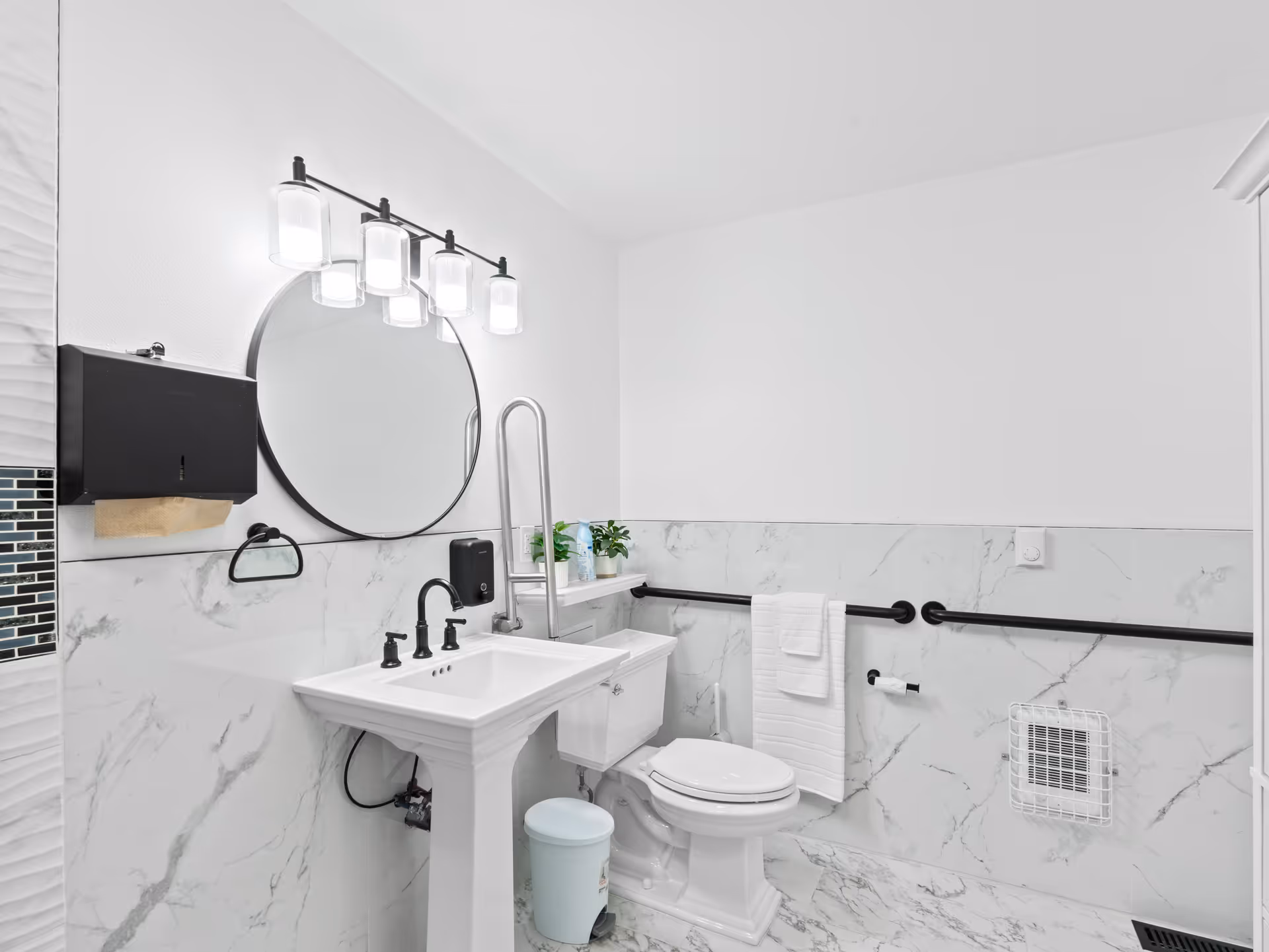 Bright, modern bathroom with pedestal sink, round mirror, and marble tiled walls.