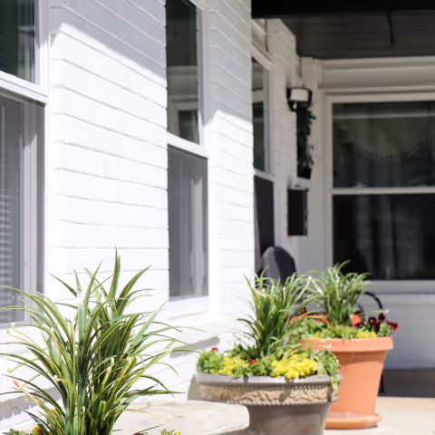 White brick exterior with windows and potted plants along a covered entrance