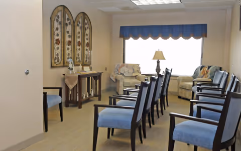 Beige waiting area with blue chairs, a sofa, and a window in a hospice lounge.