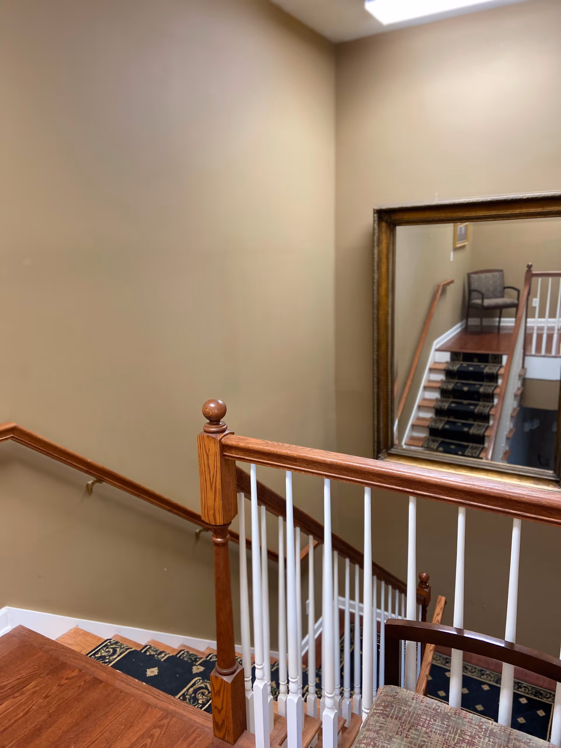 Interior stairwell with wooden handrail, beige walls, carpeted stairs, and a large framed mirror.