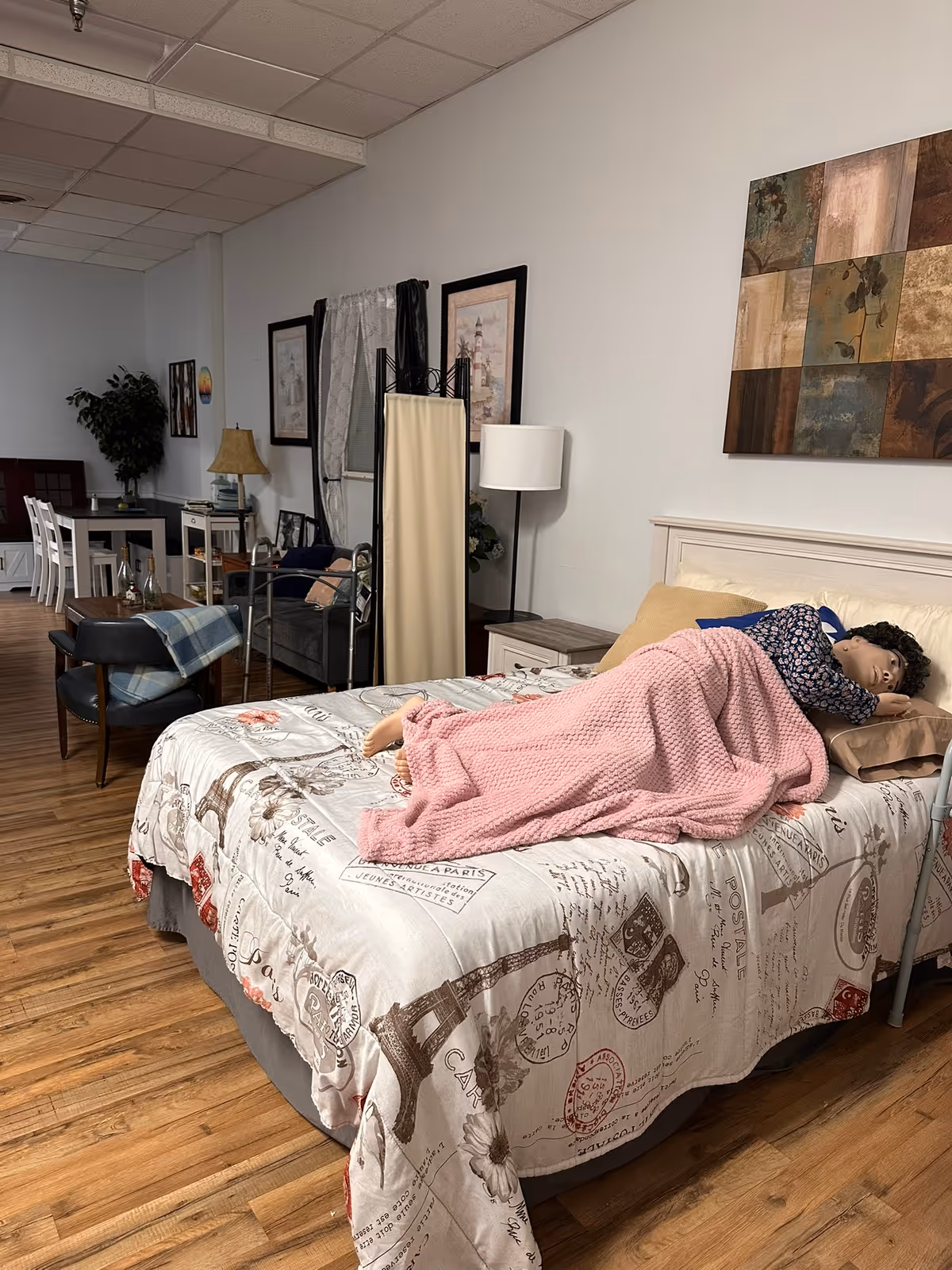 Bedroom in a senior facility with a bed, furniture, and a resident under a pink blanket.