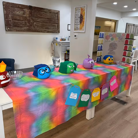 Indoor activity table with bright tie-dye cloth and colorful craft items arranged along the length.