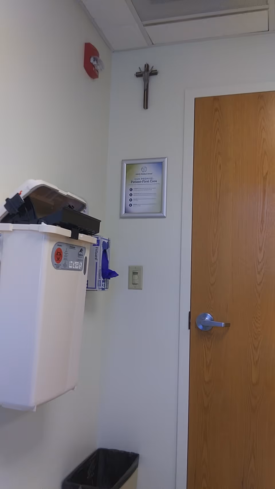 Interior hospital-like corridor showing a wooden door, crucifix, and wall equipment.