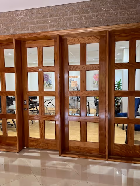Wooden-framed glass doors separate a bright interior room with chairs and plants.