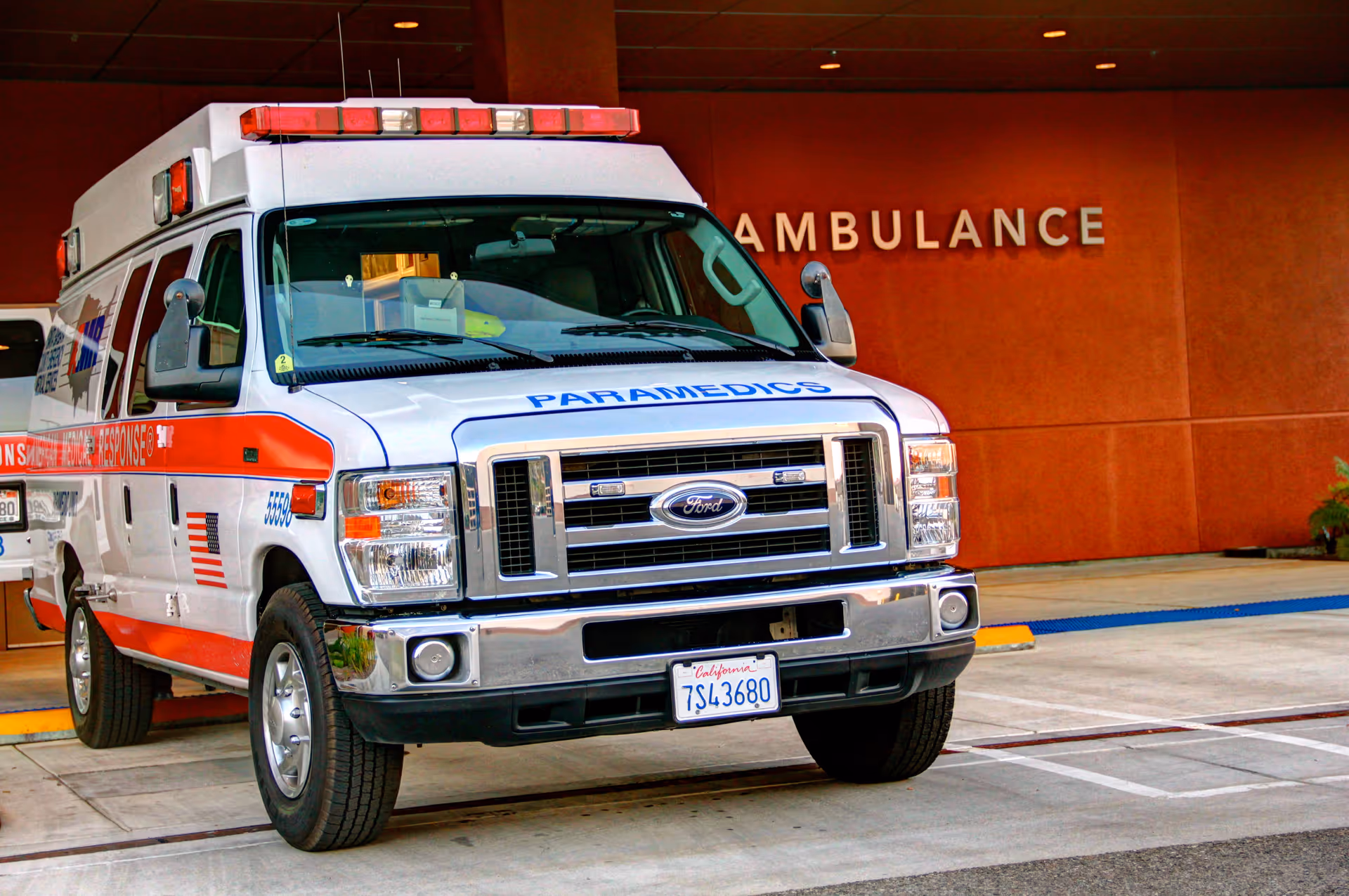 Front view of a white and red ambulance parked outside a hospital entrance.