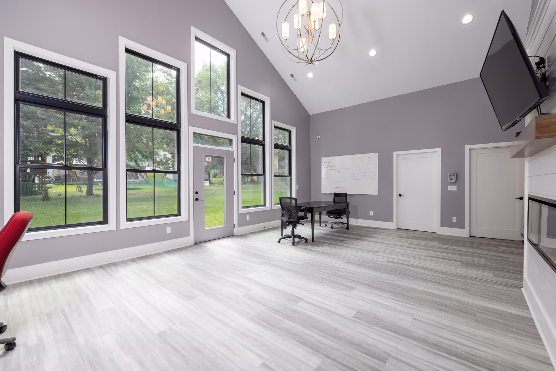 Spacious modern interior area with large windows, high ceiling, a table and chairs, and a whiteboard.