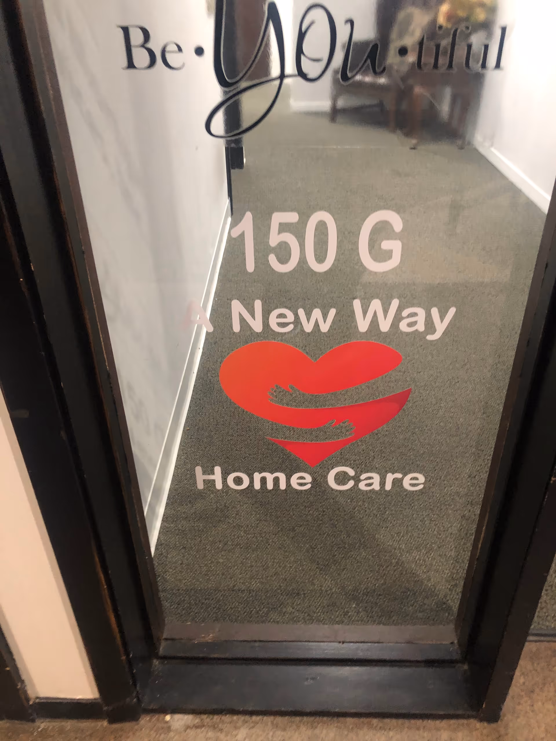 Interior hallway through glass door showing facility branding and a red heart logo.