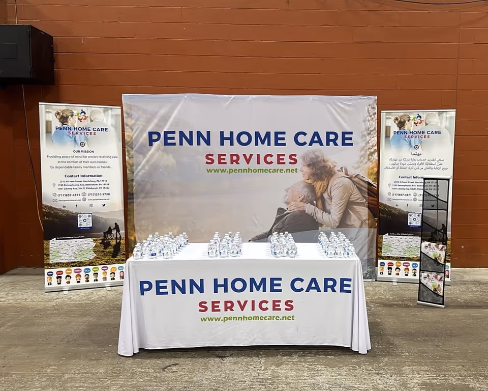 Outdoor promotional booth with Penn Home Care banners, a table of water bottles, and display stands.