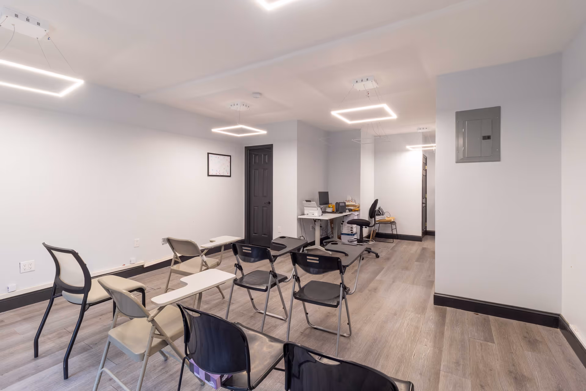 Bright, empty interior room with stacked chairs, desks, and a desk setup against the back wall.