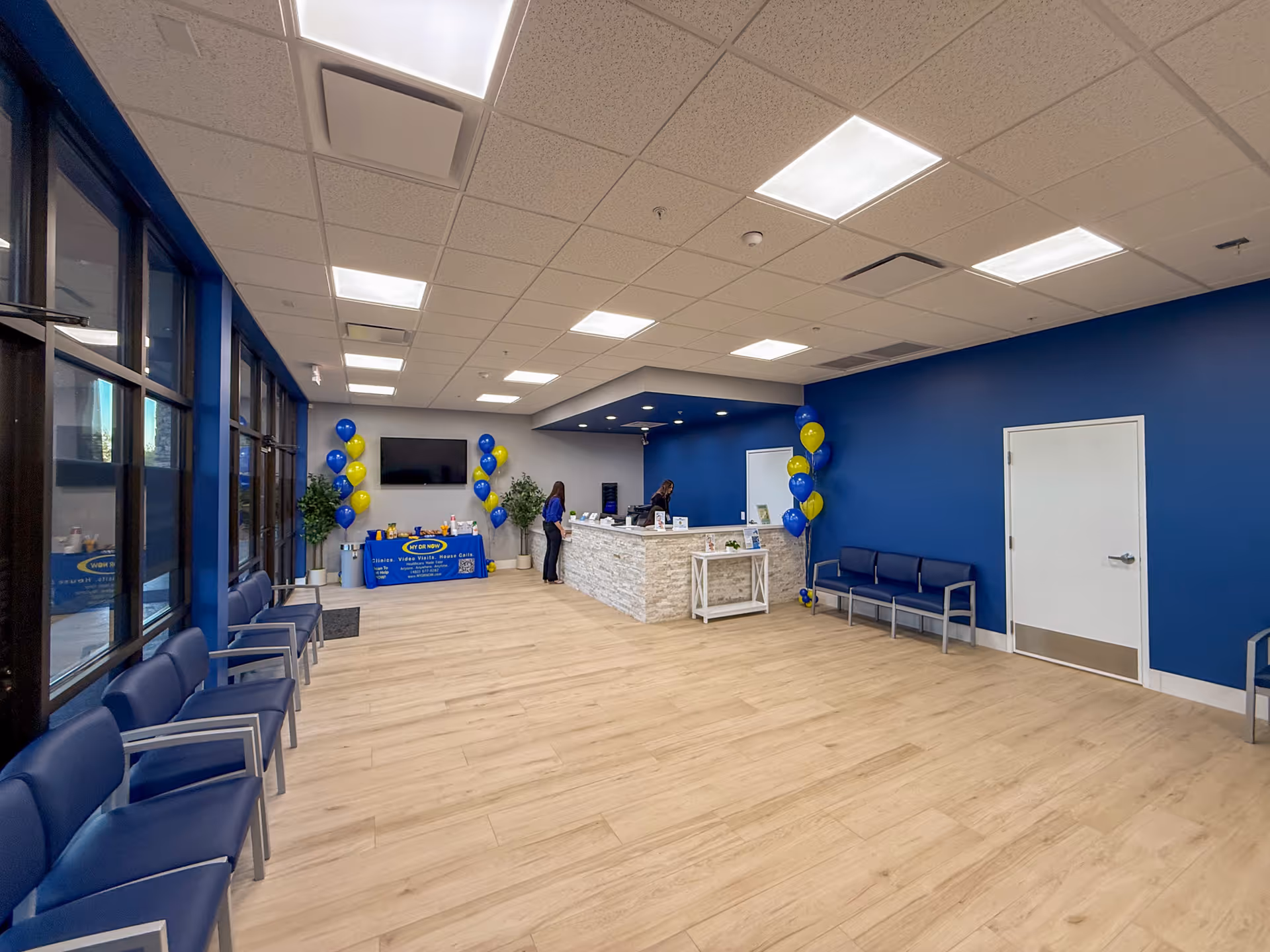 Modern indoor lobby with blue walls, arranged seating, balloons, and a reception desk.
