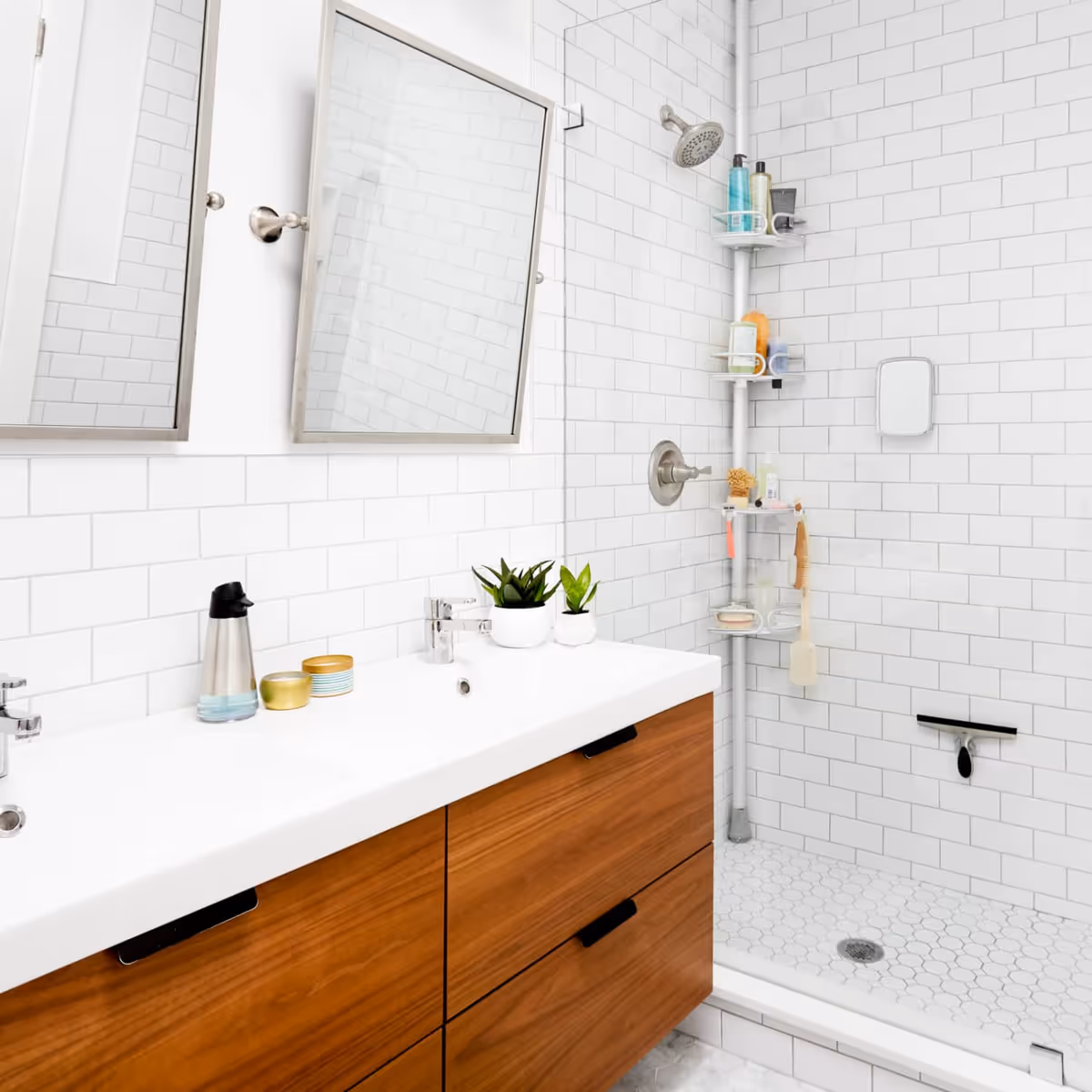 Bright white bathroom with wood vanity, mirrors, and a tiled shower stall.