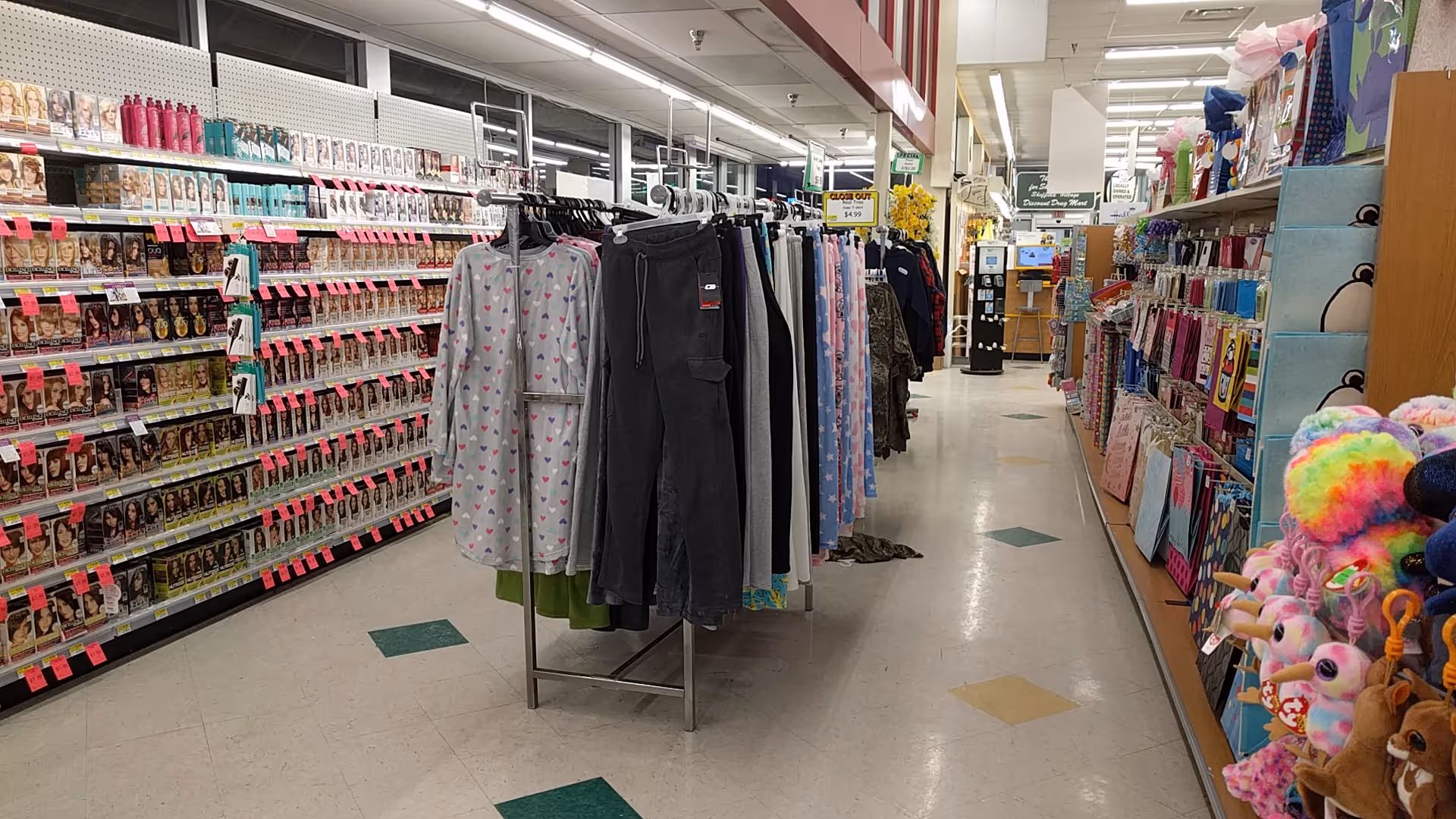 A long aisle in a Discount Drug Mart store with clothing racks and plush toys.