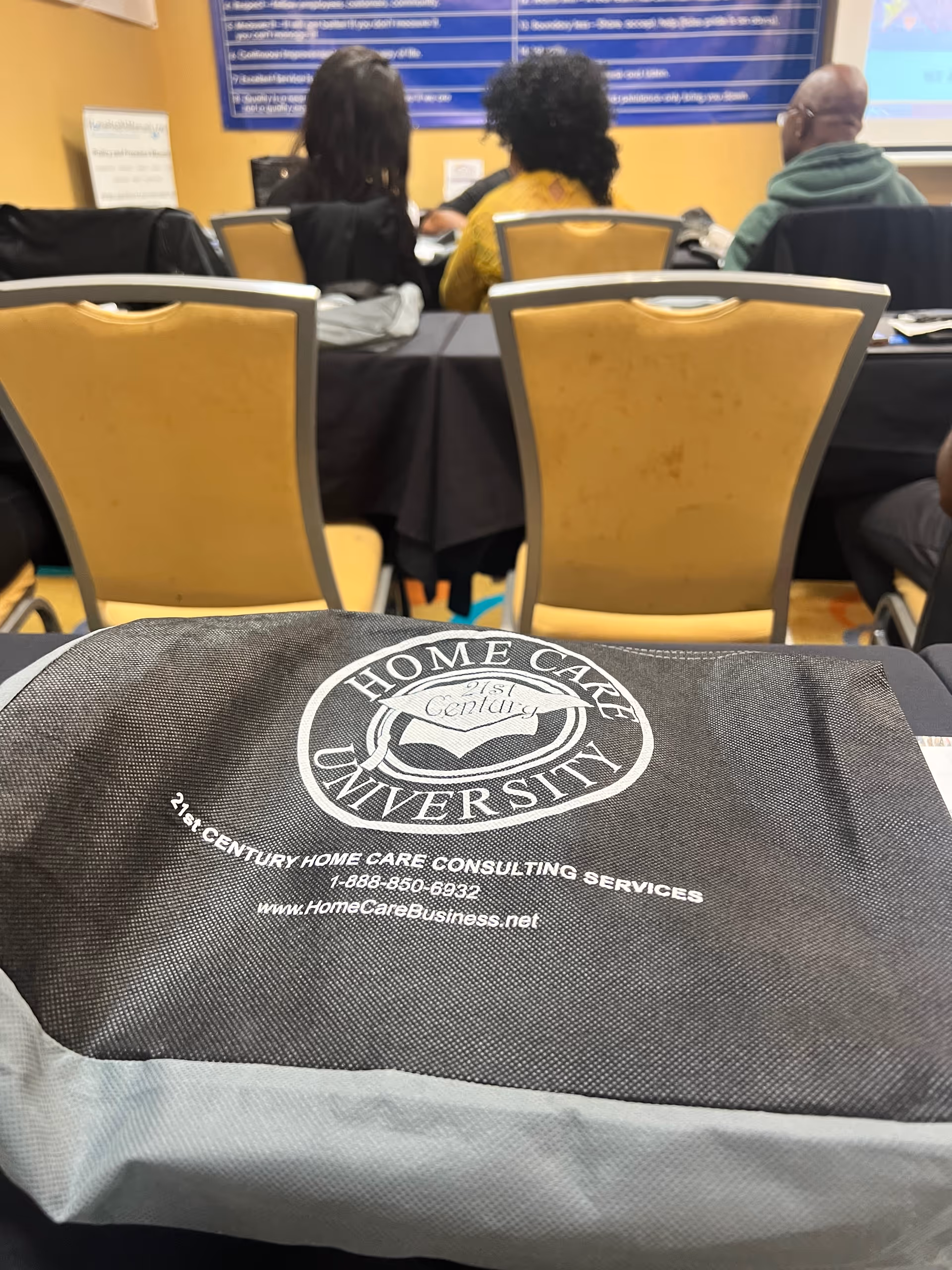 Conference room training scene with attendees and a branded home care bag in foreground.