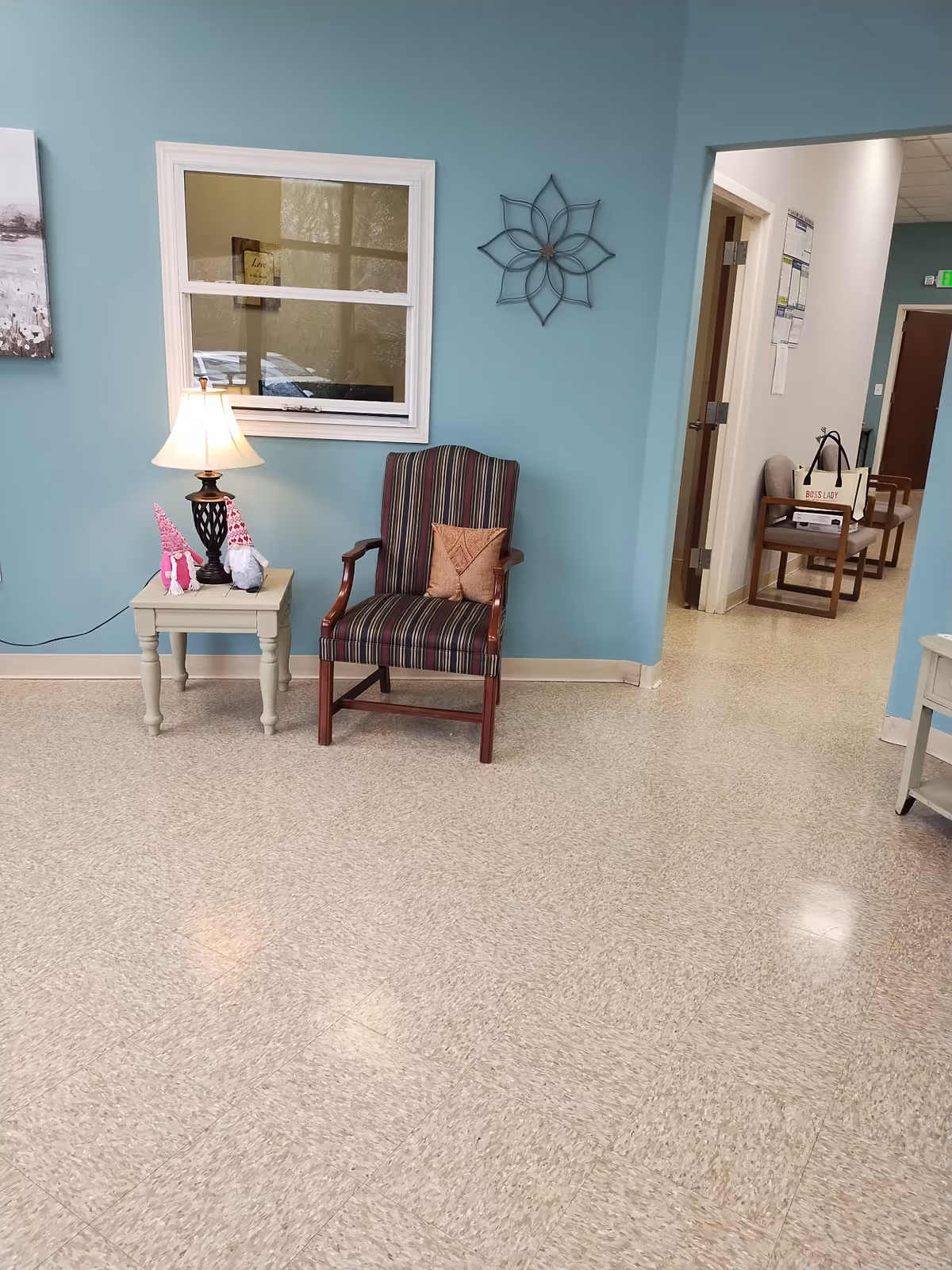 Teal-walled waiting area with striped chair, side table, lamp, and doorway to hall