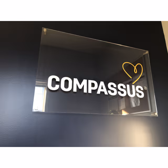 Indoor wall sign displaying COMPASSUS with a yellow outlined heart logo