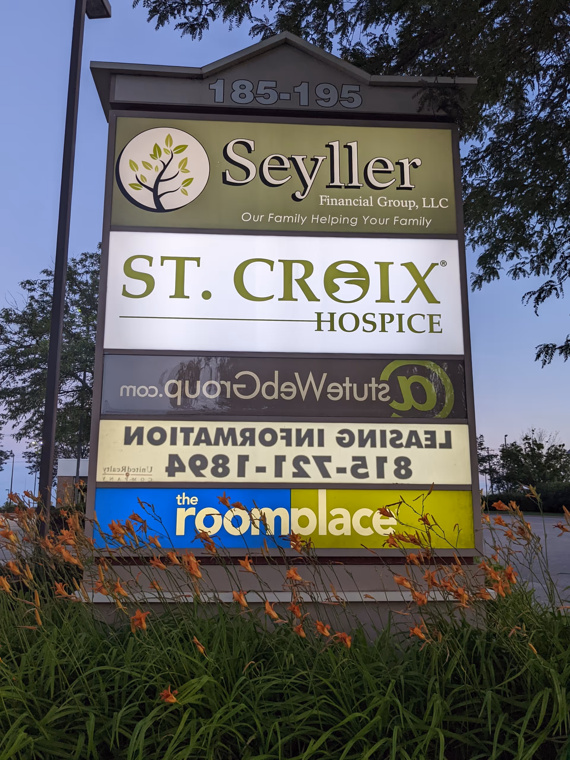 A multi-panel outdoor sign for St. Croix Hospice with other business names beneath a garden bed