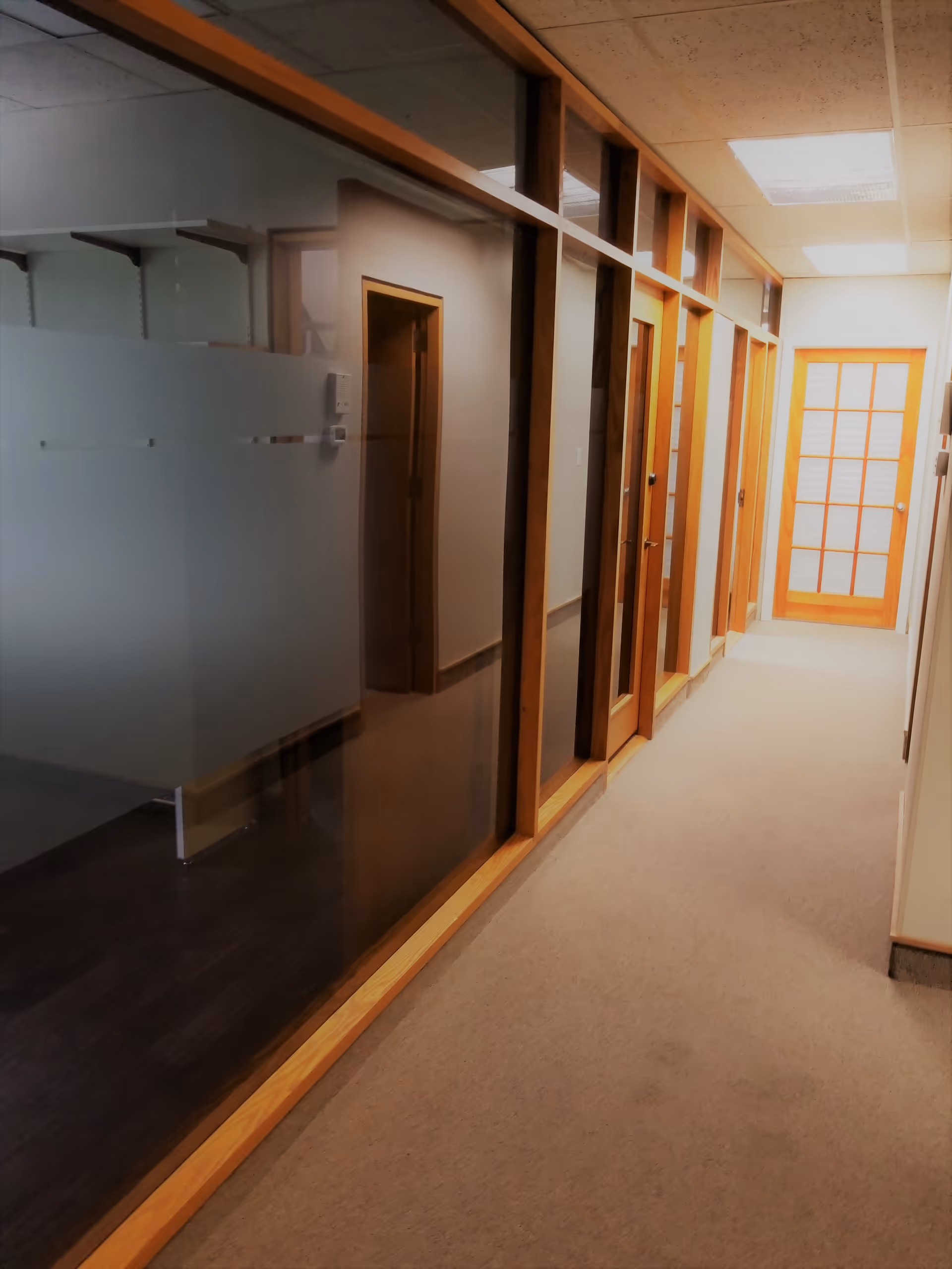 A long indoor hallway in a senior living facility with glass walls and wooden door frames.