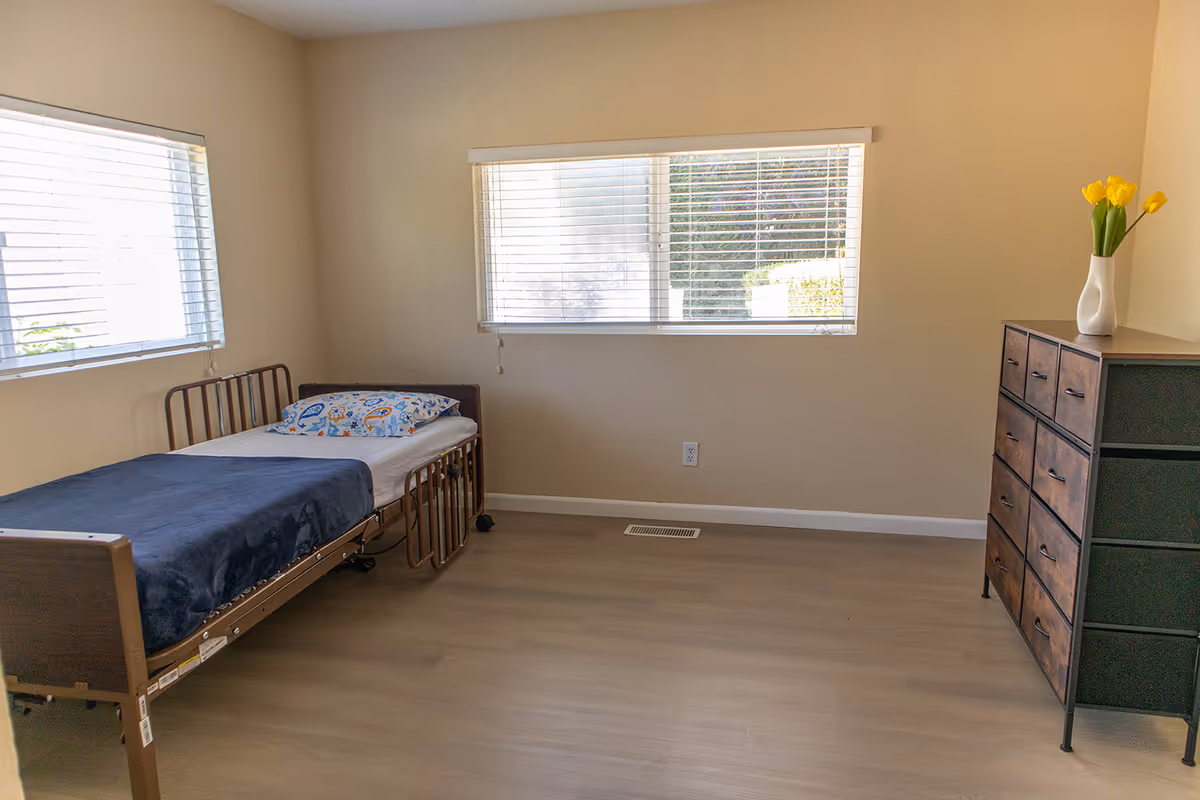 A sparsely furnished bedroom with a single bed, dresser, and yellow tulips.