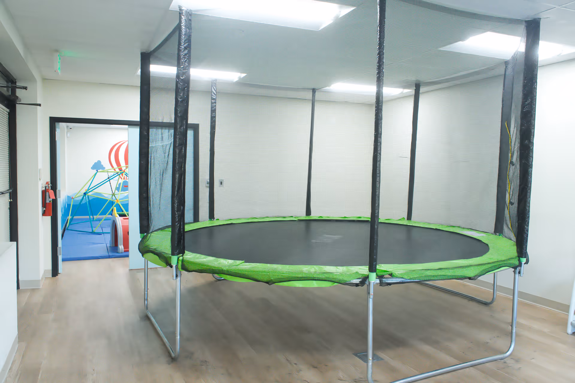 Indoor therapy room featuring a large trampoline with black netting and green padding