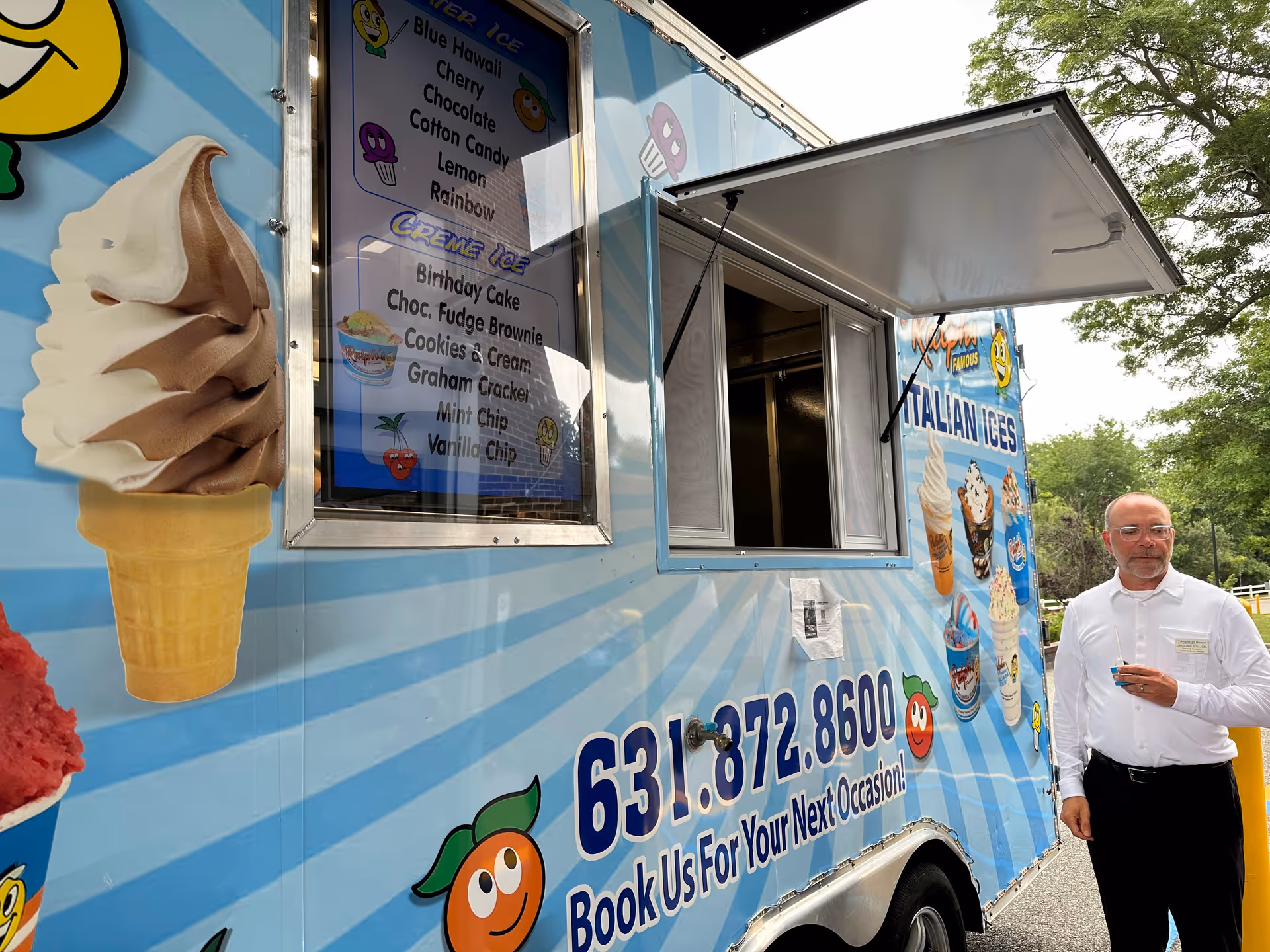Blue ice cream truck with open window and a man in a white shirt standing nearby.