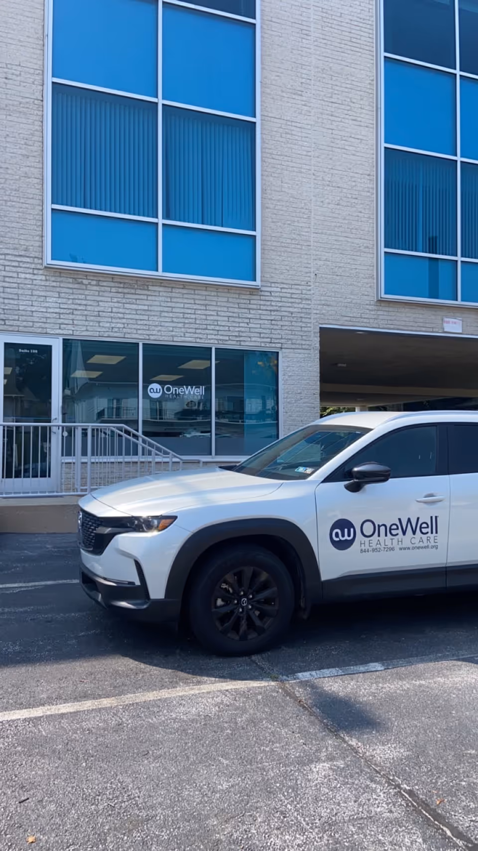 Exterior view of OneWell Health Care building with a white company SUV parked in front.