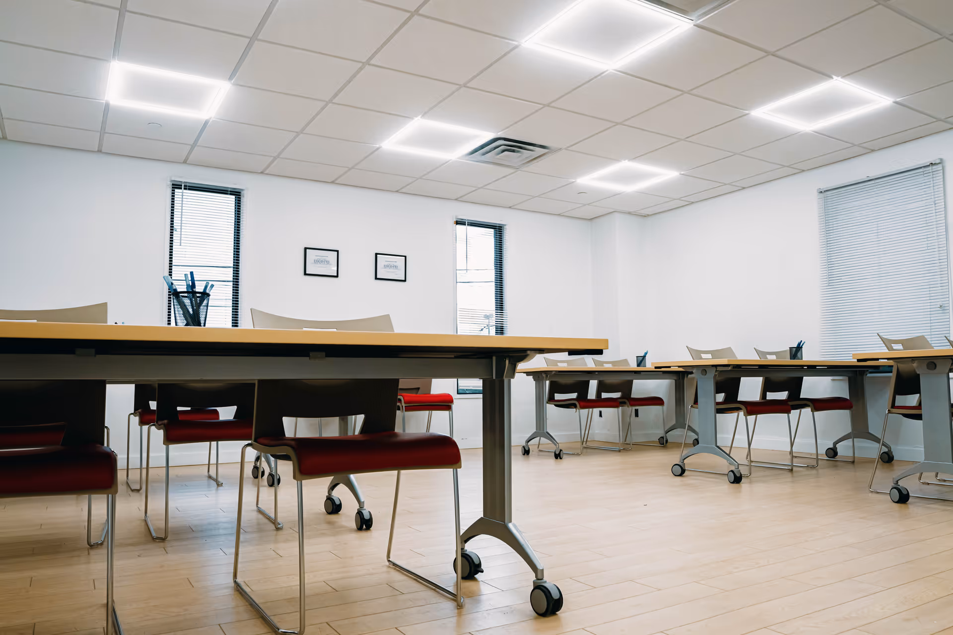 Empty multipurpose classroom with long tables, red chairs, and bright ceiling lights.