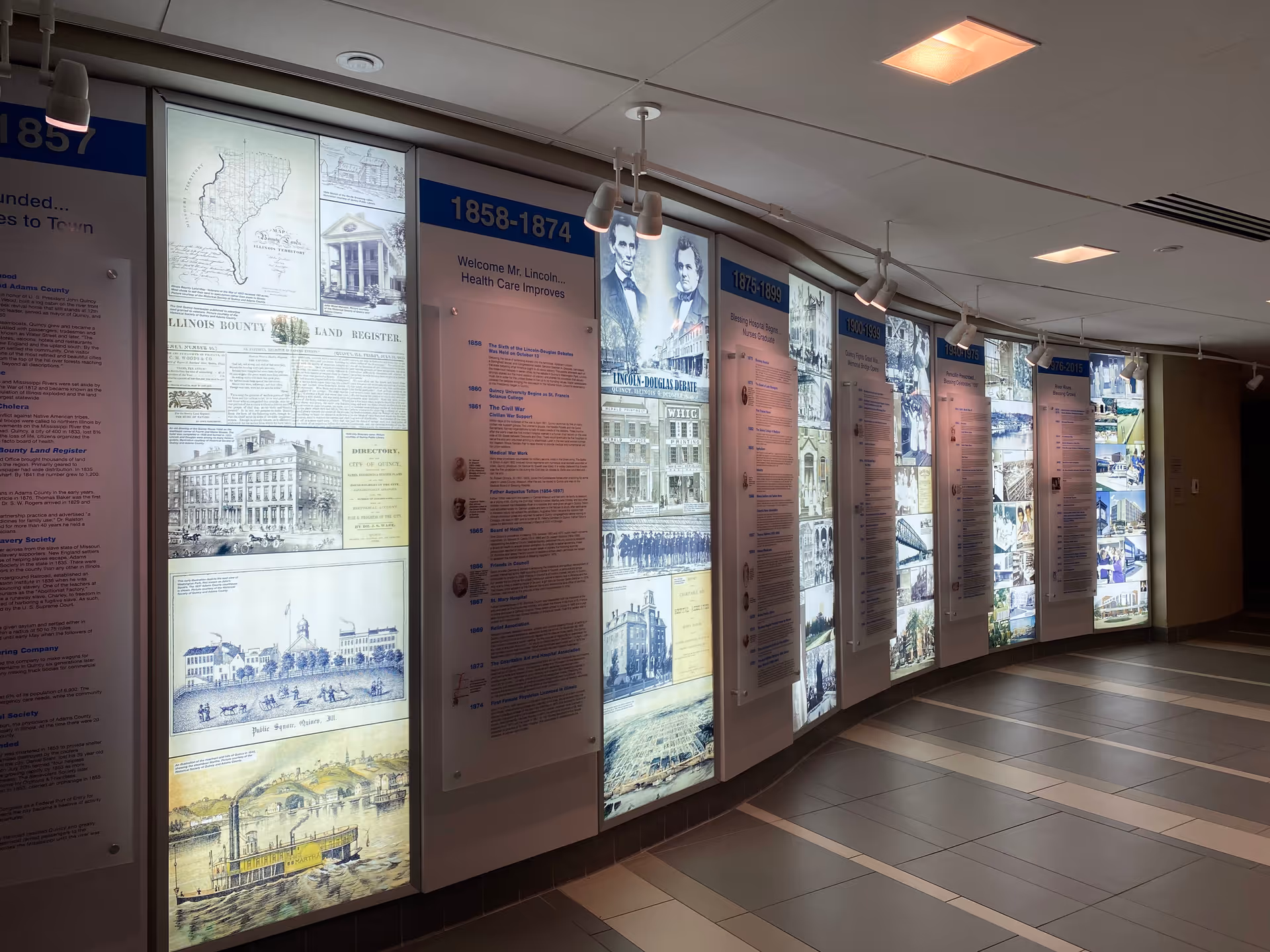 Dimly lit hospital hallway with large history display panels along curved wall.