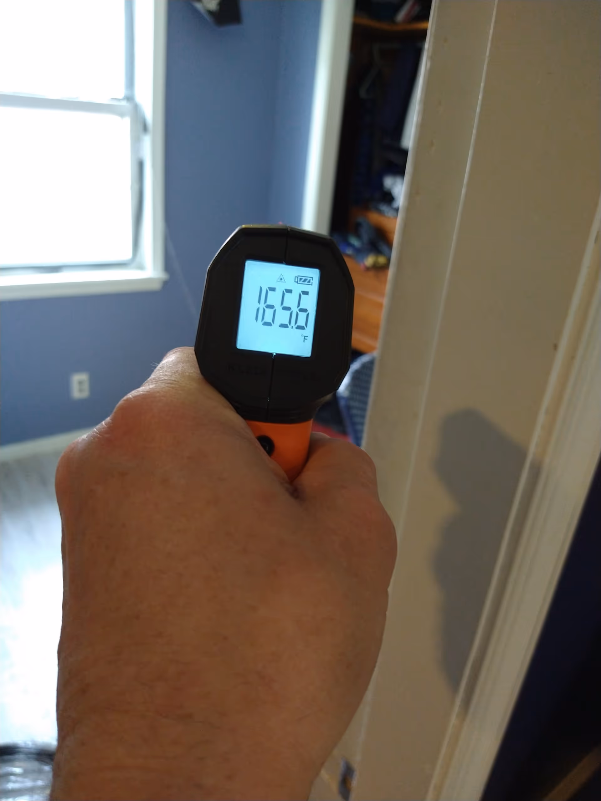 A hand holds a digital infrared thermometer displaying 165.6°F indoors.