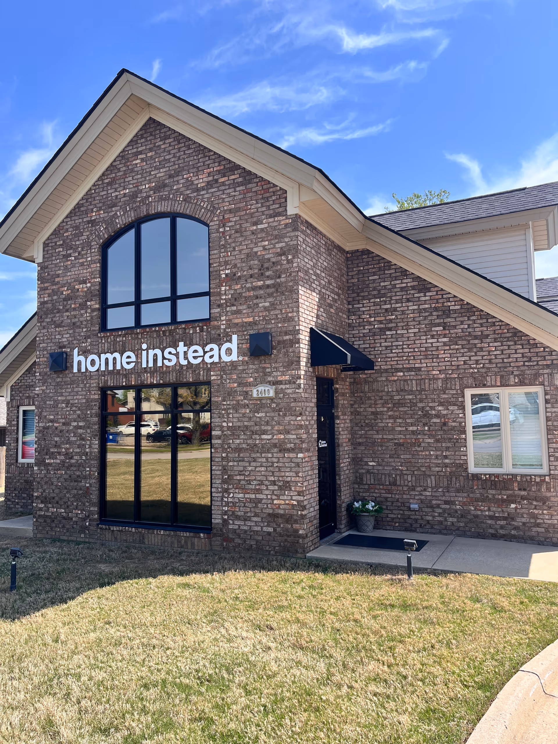 Brick exterior of a Home Instead building with a large arched window and sign.