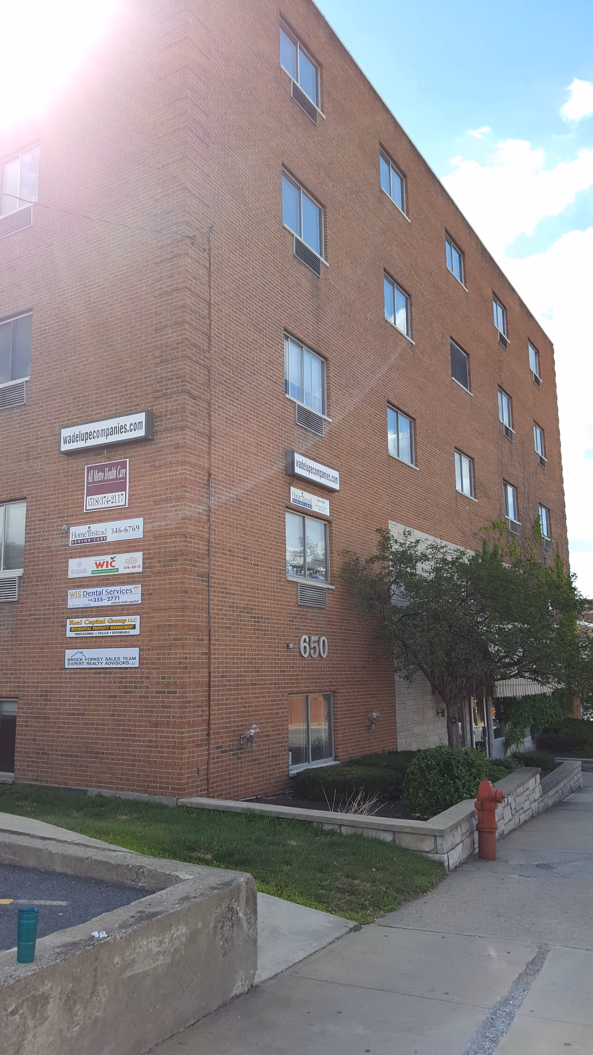 Brick mid-rise building with multiple signs on the exterior wall beside a sidewalk.